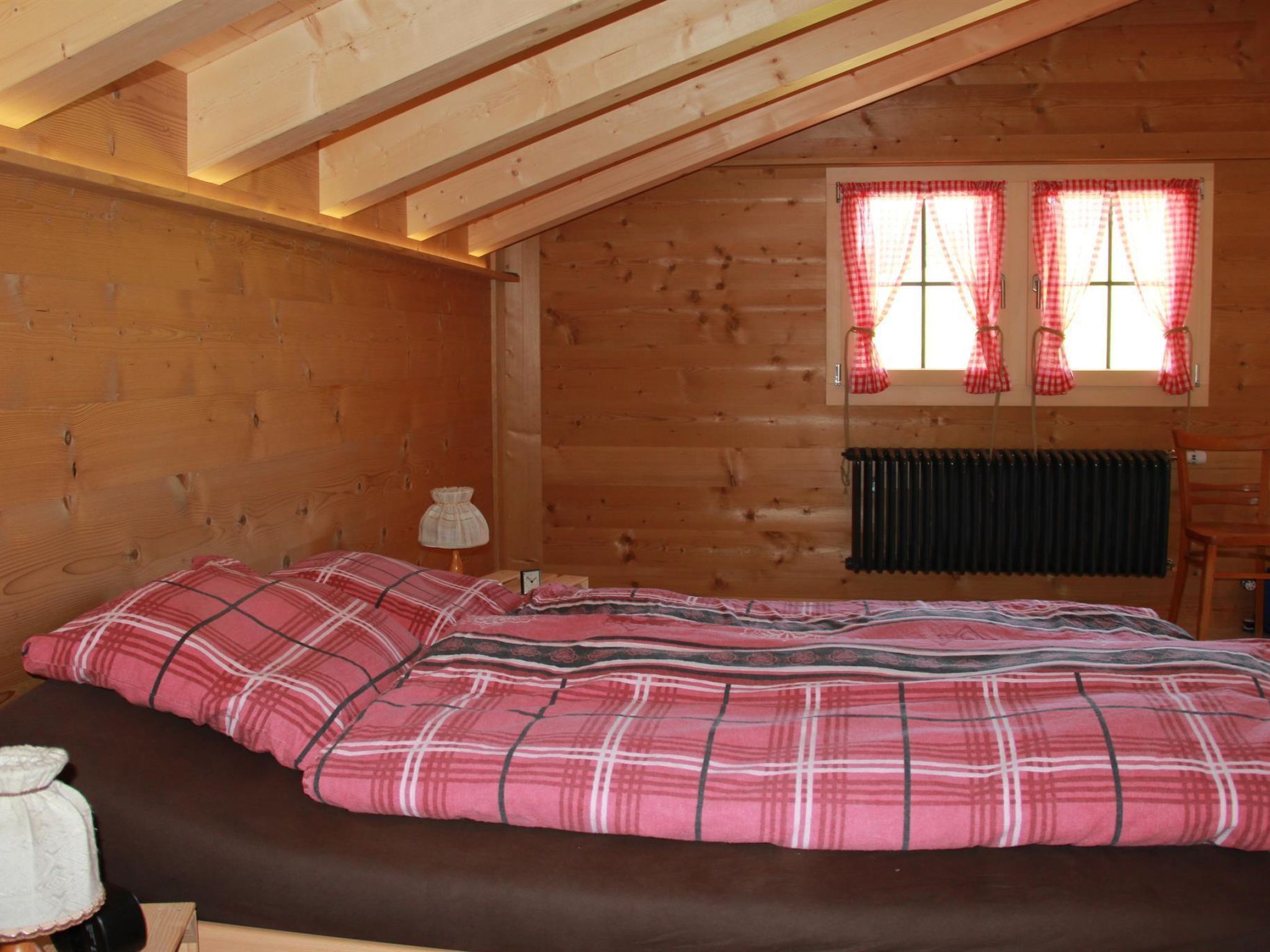 A wooden cabin bedroom with a bed, a nightstand, a lamp, and a window with curtains.