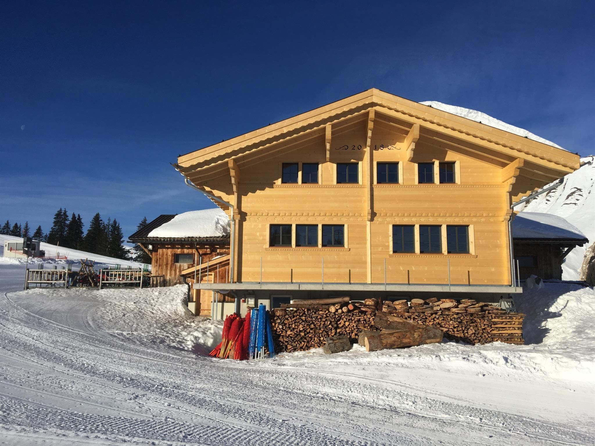 Un bâtiment en bois à deux étages, doté d’un toit plat, de grandes fenêtres et, en arrière-plan, d’une montagne enneigée.