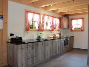Eine moderne Küche mit Holzschränken, einer schwarzen Arbeitsplatte und roten und weißen Karomustert-Vorhängen.