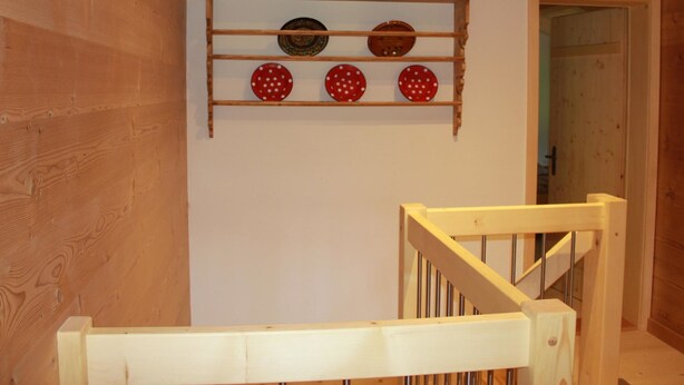 A wooden staircase with a white handrail and a wall-mounted shelf with decorative plates. - Alphaus Hasler Appartement/Fewo, Dusche, WC, 4 oder mehr Schlafräume by Interhome (Lenk)