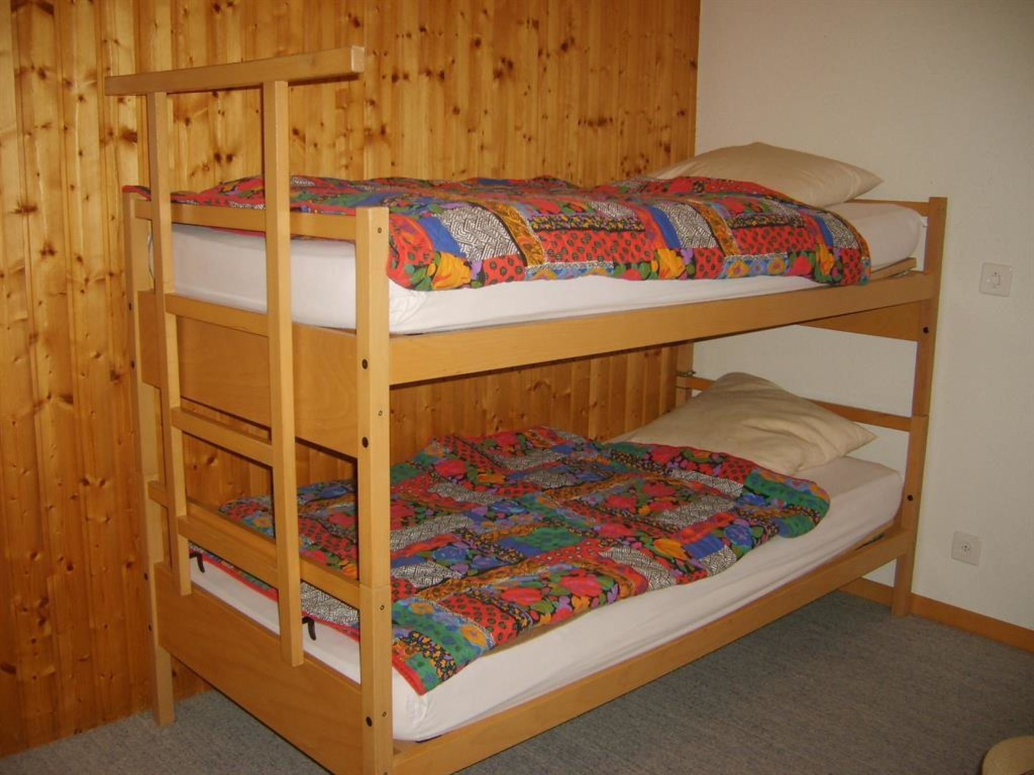 Eine Etagenbett mit zwei Schlafstellen, jeweils mit einer Matratze und einer farbenfrohen Decke.
