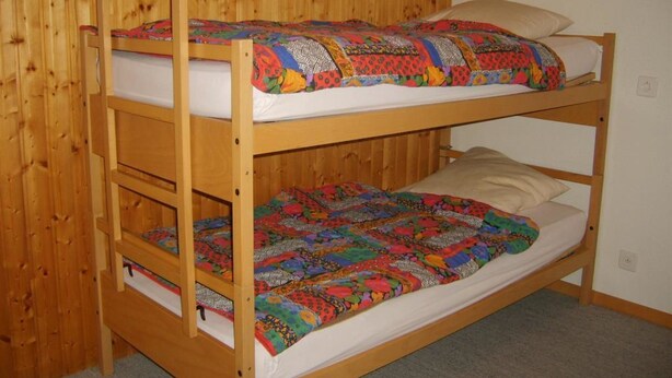 A bunk bed with two levels, each with a mattress and a colorful quilt. - Arnika # 1 Appartement/Fewo, Dusche oder Bad, WC, 1 Schlafraum by Interhome (Lenk)