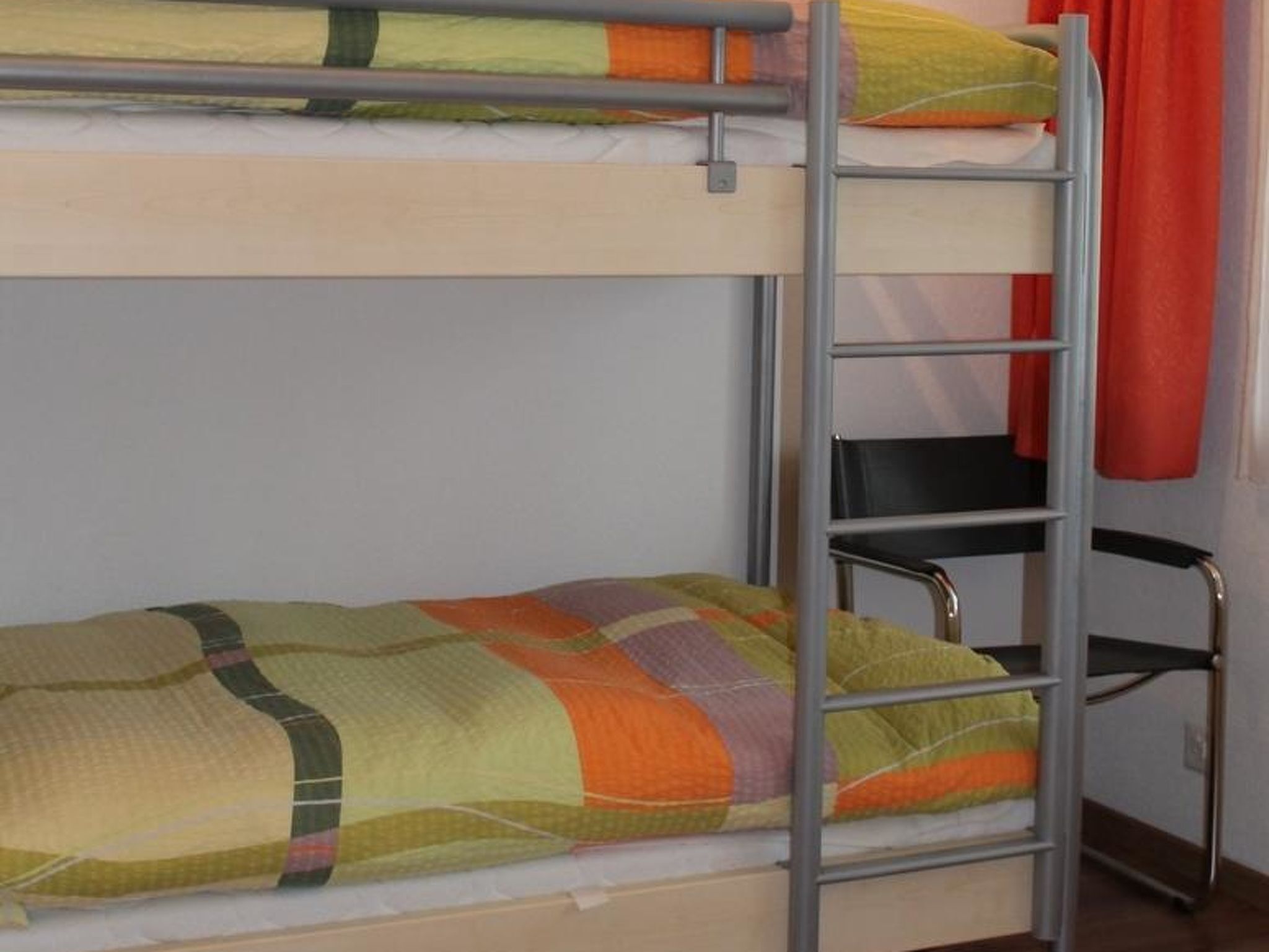 Ein Stockbett mit einer Leiter, einem Stuhl und einem roten Vorhang.