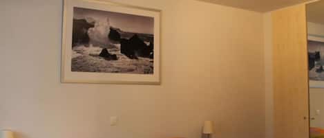 Une chambre à coucher avec un lit, deux lampes de chevet, un tableau encadré au mur et une porte donnant sur une autre pièce.