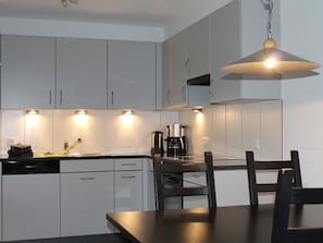 A modern kitchen with white cabinets, a black countertop, and a dining table with chairs. - Rawilstrasse 33 Appartement/Fewo, Dusche oder Bad, WC, 2 Schlafräume by Interhome (Lenk)