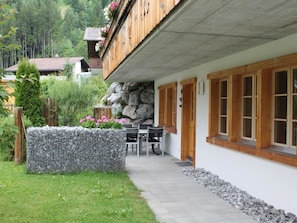 A two-story wooden building with a stone wall and a garden area with a table and chairs. - Rawilstrasse 33 Appartement/Fewo, Dusche oder Bad, WC, 2 Schlafräume by Interhome (Lenk)