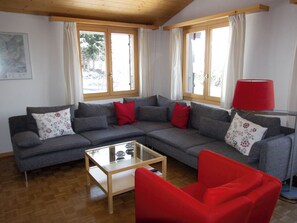 A living room with a grey sectional sofa, red armchairs, a glass coffee table, and a red floor lamp. - Möösli Appartement/Fewo, Dusche oder Bad, WC, 4 oder mehr Schlafräume by Interhome (Lenk)