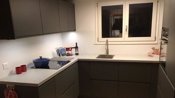 Una cocina compacta con armarios oscuros, una encimera blanca, un lavamanos y una ventana arriba.