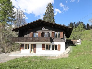 A two-story wooden house with a balcony, set in a grassy area with trees in the background. - Möösli Appartement/Fewo, Dusche oder Bad, WC, 4 oder mehr Schlafräume by Interhome (Lenk)