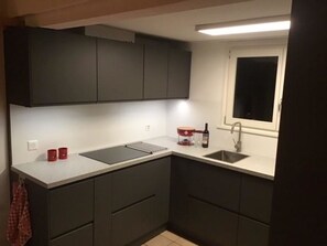 A compact kitchen with dark cabinets, a countertop, a sink, and a window. - Möösli Appartement/Fewo, Dusche oder Bad, WC, 4 oder mehr Schlafräume by Interhome (Lenk)