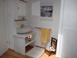 A bathroom with a sink, mirror, towel rack, and a painting on the wall. - Chalet Weitblick Appartement/Fewo, Dusche oder Bad, WC, Balkon by Interhome (Lenk)