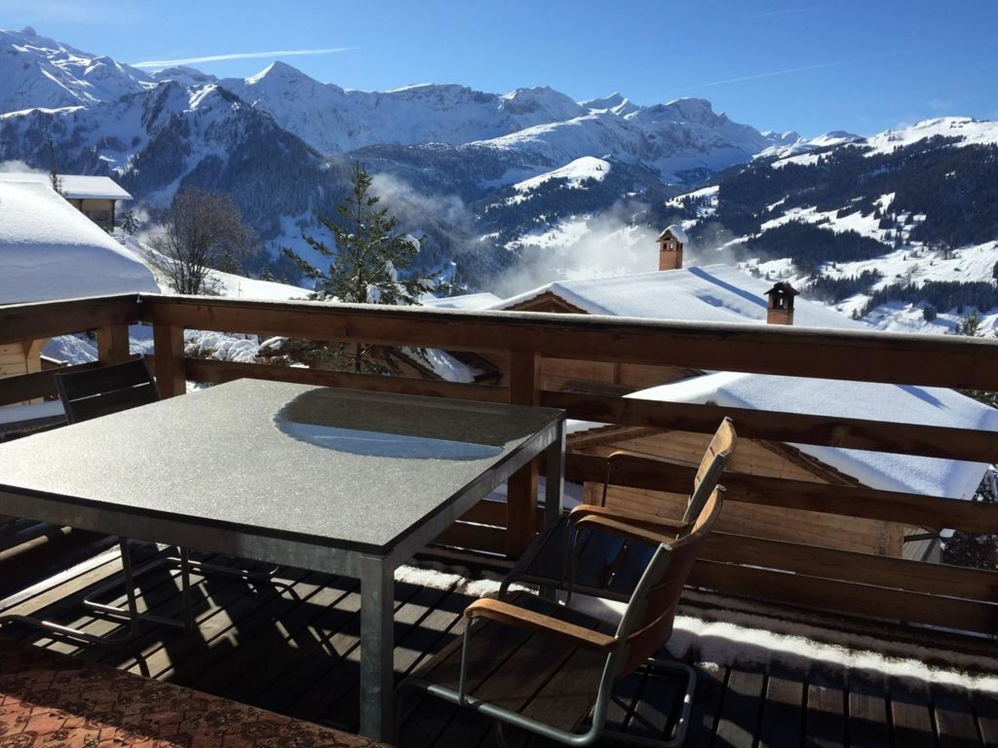 Een terras met een tafel en stoelen, met uitzicht op besneeuwde bergen.
