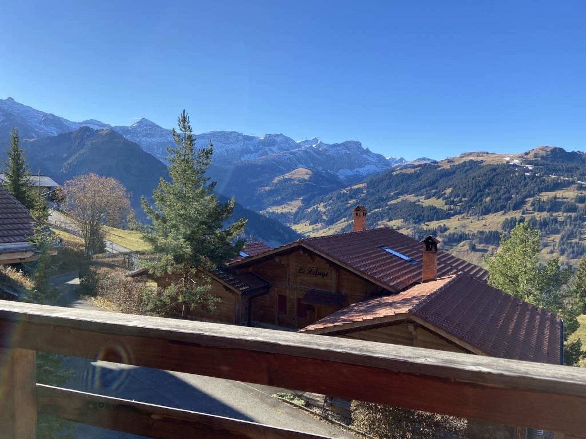 A mountain cabin with a red roof, surrounded by trees and mountains.