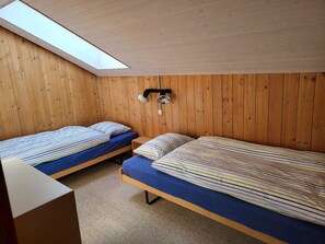 Et værelse med to senge, trævægge, et ovenlys og en lampe i loftet.