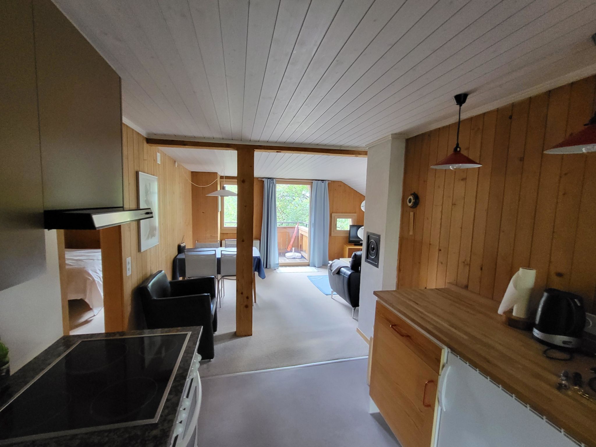 A compact kitchen with a dining area, wooden walls, and a view to an outdoor balcony.