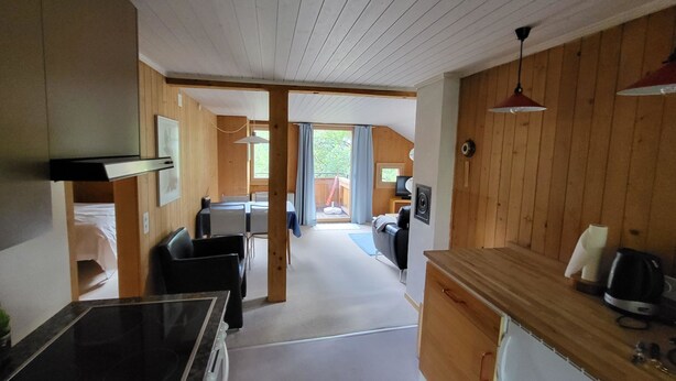 A compact kitchen with a dining area, wooden walls, and a view to an outdoor balcony. - Wildbach Appartement/Fewo, Dusche oder Bad, WC, 2 Schlafräume 4-Bett-Wohnung by Interhome (Lenk)