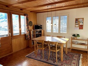 Ein Holzinterieur mit einem Esstisch, Stühlen, einem Fernseher und einer Pinwand.