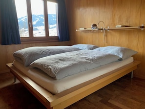 Ein Einzelbett mit Holzbettrahmen und Matratze, eine Holzvertäfelung und ein Fenster mit Vorhängen.