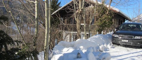 A snow-covered driveway leading to a wooden cabin with a car parked in front.