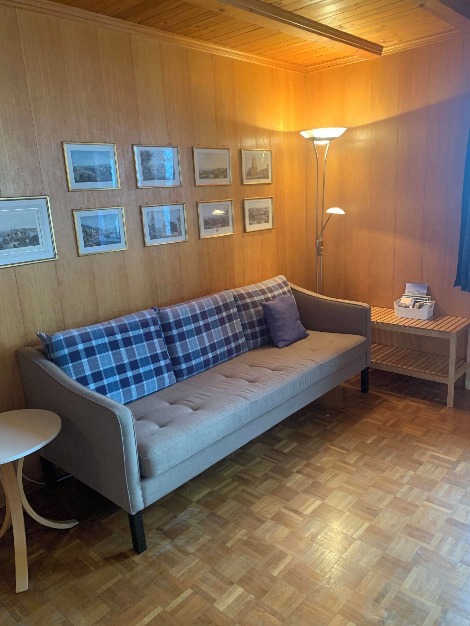 Una habitación con un sofá, una mesita, una lámpara de pie y cuadros en la pared.