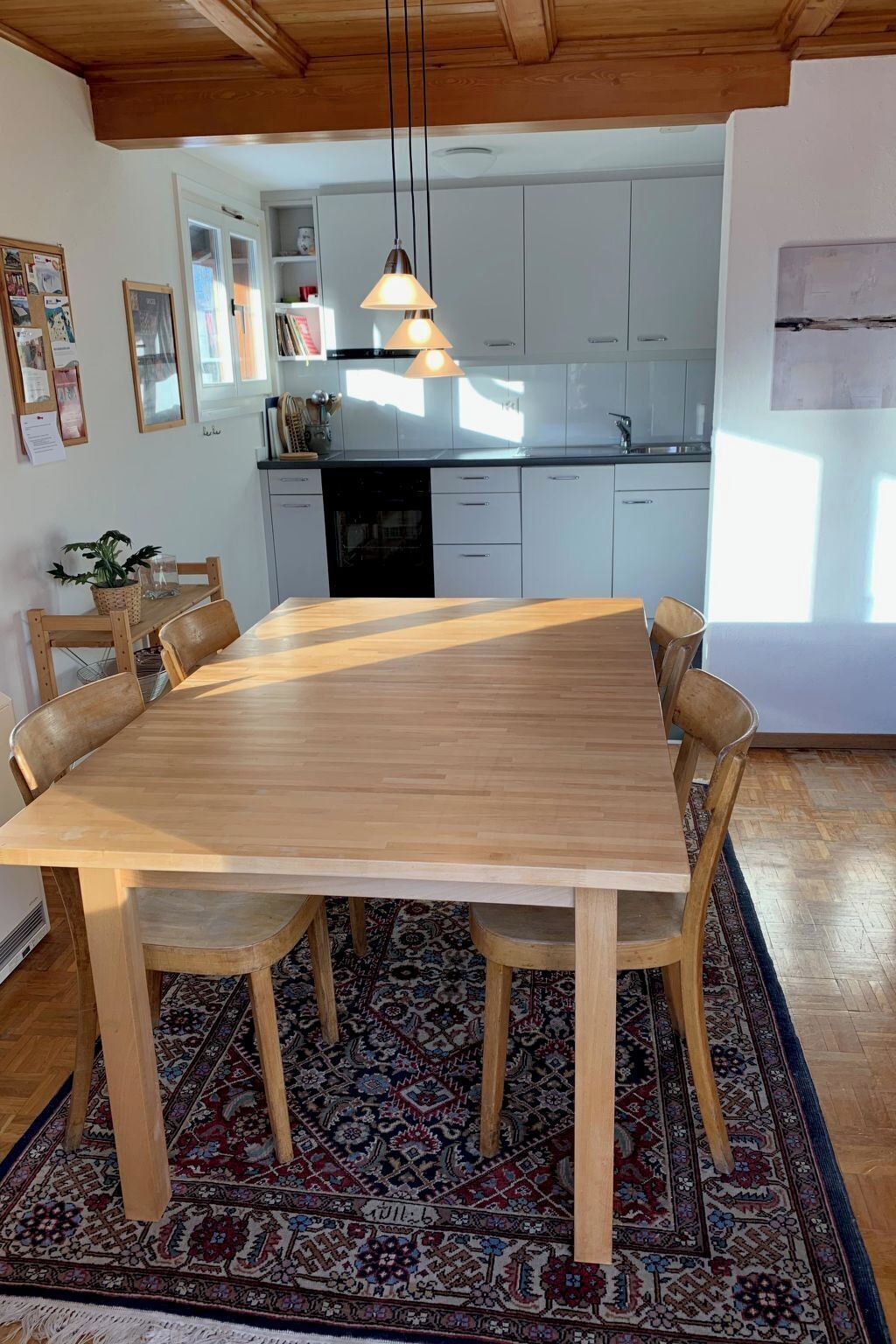 Ein Essbereich mit Holztisch und -stühlen, einem gemusterten Teppich und einer Küche im Hintergrund.