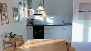 Et spiseområde med et træbord og stole, et mønstret tæppe og et køkken i baggrunden.