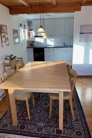 Ein Essbereich mit Holztisch und -stühlen, einem gemusterten Teppich und einer Küche im Hintergrund.