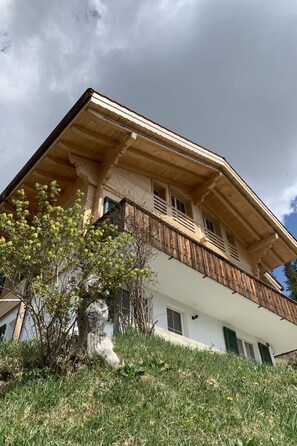 A two-story wooden building with a balcony, surrounded by grass and a small tree. - Meieli Appartement/Fewo, Dusche oder Bad, WC, 1 Schlafraum 2-Bett-Wohnung by Interhome (Lenk)