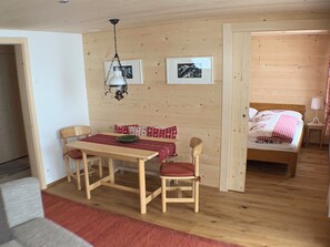 A wooden interior with a dining table, chairs, a bed, and a hanging light fixture. - Meieli Appartement/Fewo, Dusche oder Bad, WC, 1 Schlafraum 2-Bett-Wohnung by Interhome (Lenk)
