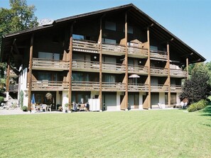 Ein mehrstöckiges Gebäude mit Balkonen, einer flachen Dachterrasse und einer Rasenfläche vor der Fassade.
