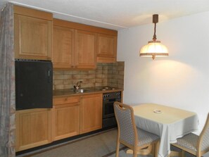 Eine kleine Küche mit Holzausstattung, einem schwarzen Kühlschrank, einem Herd und einem Esstisch mit zwei Stühlen.