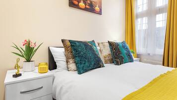 A hotel room with a bed, a nightstand, a potted plant, a candle, and a window with curtains.
