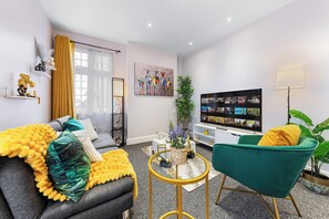 A modern living room with a sofa, armchair, TV, and decorative items. - Immaculate 2-Bedroom London Flat | King Bed | Sleeps 6 | Parking Available (Barnet)