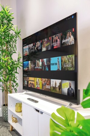 A flat-screen TV mounted on a white entertainment unit with a remote control on top. - Immaculate 2-Bedroom London Flat | King Bed | Sleeps 6 | Parking Available (Barnet)