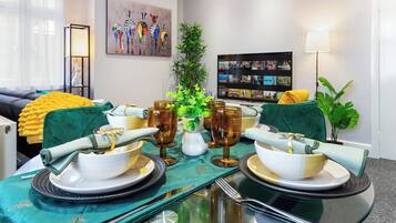 A dining table set with plates, bowls, glasses, and cutlery, surrounded by chairs with cushions.