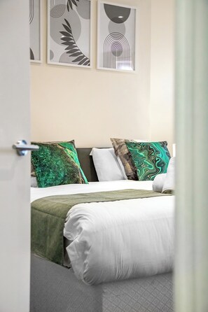 A neatly made bed with a green and white bedspread, two pillows with green and brown patterns, and a grey headboard. - Immaculate 2-Bedroom London Flat | King Bed | Sleeps 6 | Parking Available (Barnet)