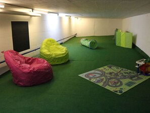 A room with green carpet, a red bean bag chair, a yellow bean bag chair, a green tunnel play structure, and a play mat with a cityscape design. - am Lee Appartement/Fewo, Dusche und Bad, WC, 2 Schlafräume 6-Bettwohnung by Interhome (Lenk)