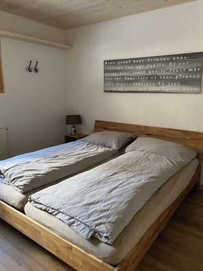 A bedroom with two single beds, a nightstand with a lamp, and a wall-mounted light fixture. - am Lee Appartement/Fewo, Dusche und Bad, WC, 2 Schlafräume 6-Bettwohnung by Interhome (Lenk)