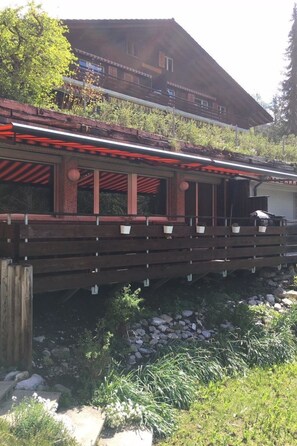 A wooden deck with potted plants, a stone pathway, and a building with a sloped roof in the background. - am Lee Appartement/Fewo, Dusche und Bad, WC, 2 Schlafräume 6-Bettwohnung by Interhome (Lenk)