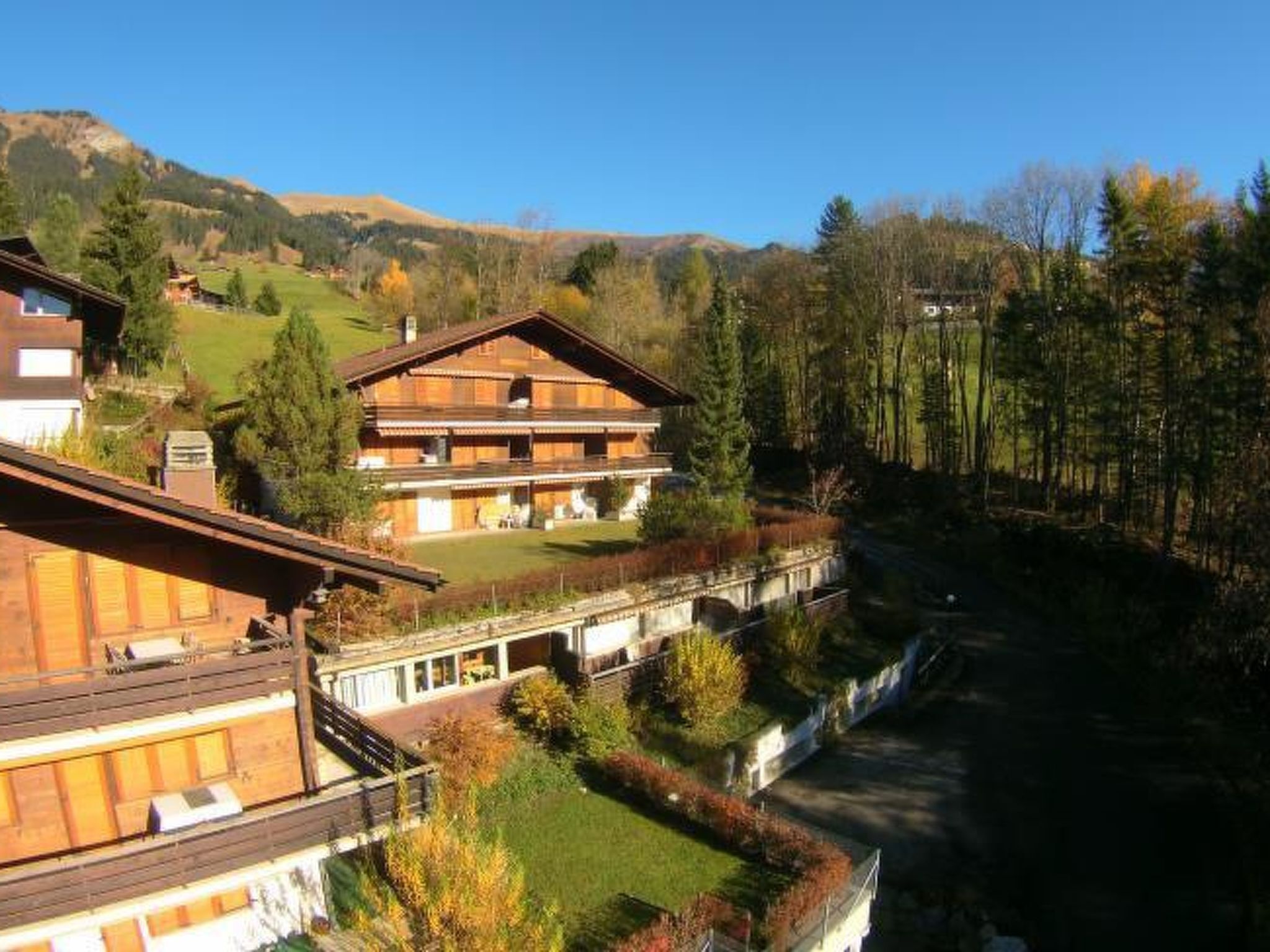 A large wooden building with multiple balconies, surrounded by a well-maintained garden and a forested hillside.