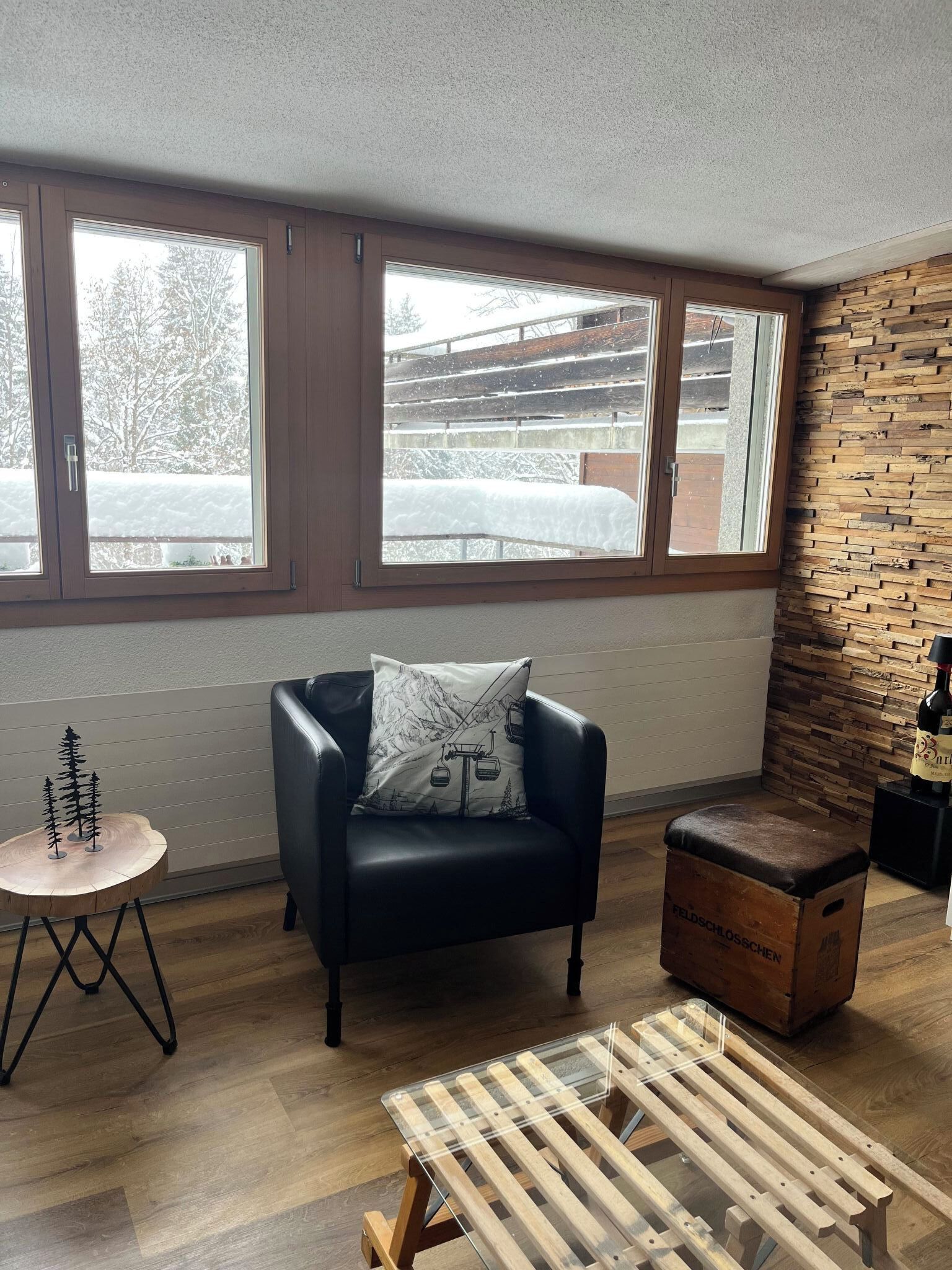 A modern living room with a black leather chair, a wooden coffee table, and a ski lift pillow.