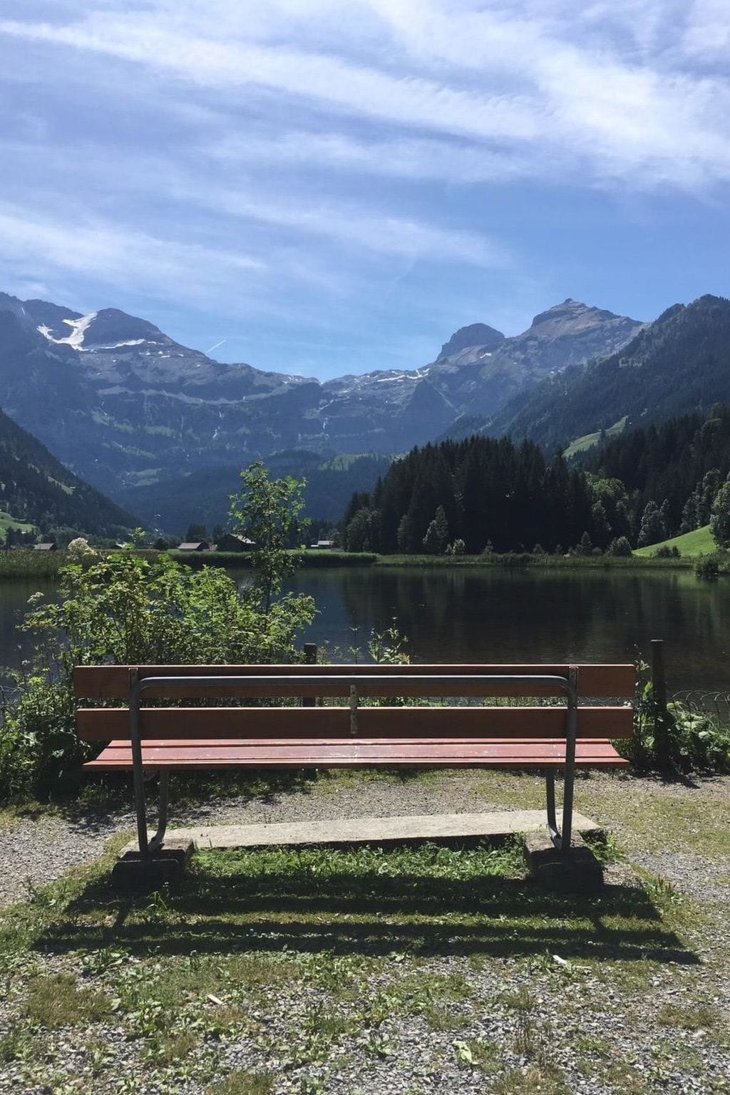 Un banc au bord d’un lac, avec des montagnes en arrière-plan.