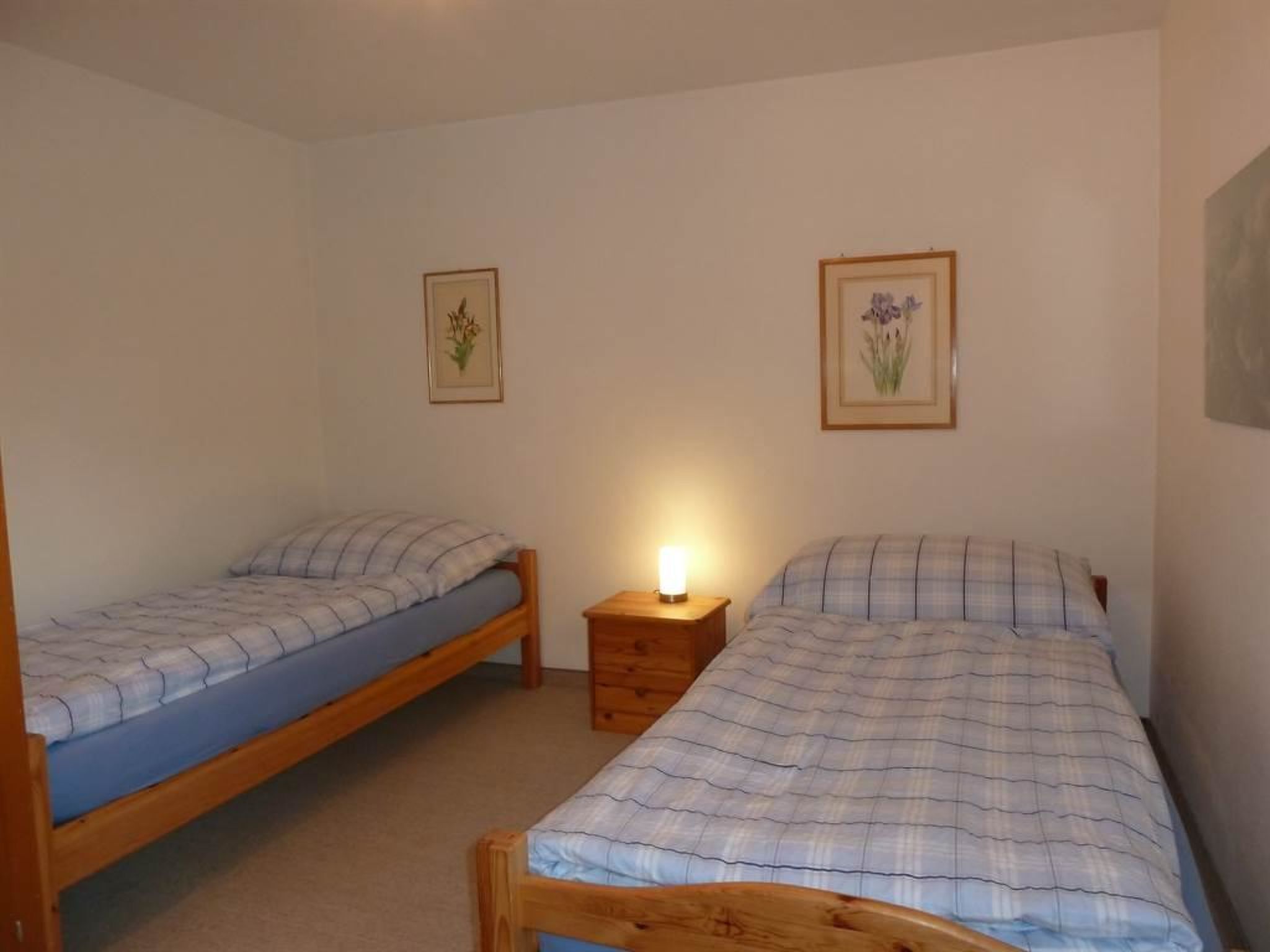 Ein Schlafzimmer mit zwei Einzelbetten, einem Nachttisch mit Lampe sowie zwei gerahmten Blumenbildern an der Wand.