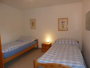 A bedroom with two single beds, a nightstand with a lamp, and two framed floral pictures on the wall. - Bach Appartement/Fewo, Dusche oder Bad, WC, 1 Schlafraum 2-Bett-Wohnung by Interhome (Lenk)