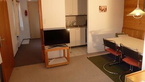 A compact living space with a kitchenette, a dining area with a table and chairs, and a television on a stand. - Bach Appartement/Fewo, Dusche oder Bad, WC, 1 Schlafraum 2-Bett-Wohnung by Interhome (Lenk)