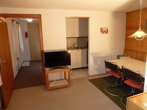 A compact living space with a kitchenette, a dining area with a table and chairs, and a television on a stand. - Bach Appartement/Fewo, Dusche oder Bad, WC, 1 Schlafraum 2-Bett-Wohnung by Interhome (Lenk)