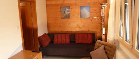 Et hyggeligt rum med trævæg, sofa, stol og skab.