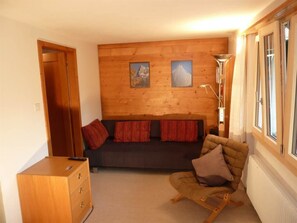 A cozy room with a wooden wall, a sofa, a chair, and a cabinet. - Bach Appartement/Fewo, Dusche oder Bad, WC, 1 Schlafraum 2-Bett-Wohnung by Interhome (Lenk)