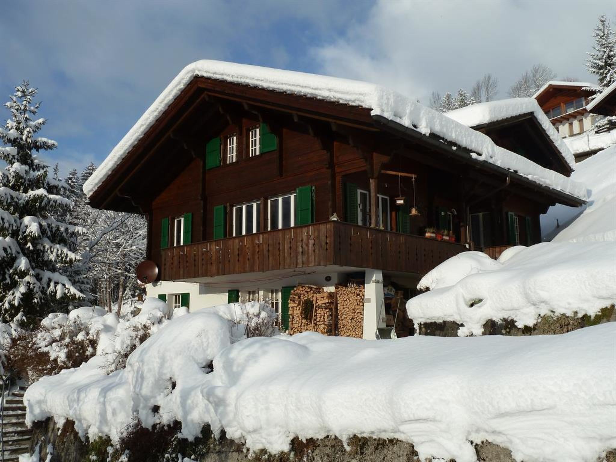 A wooden chalet with a balcony, surrounded by snow-covered trees.