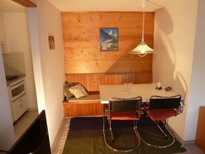A compact room with a wooden wall, a bench, a table with chairs, and a hanging light fixture. - Bach Appartement/Fewo, Dusche oder Bad, WC, 1 Schlafraum 2-Bett-Wohnung by Interhome (Lenk)